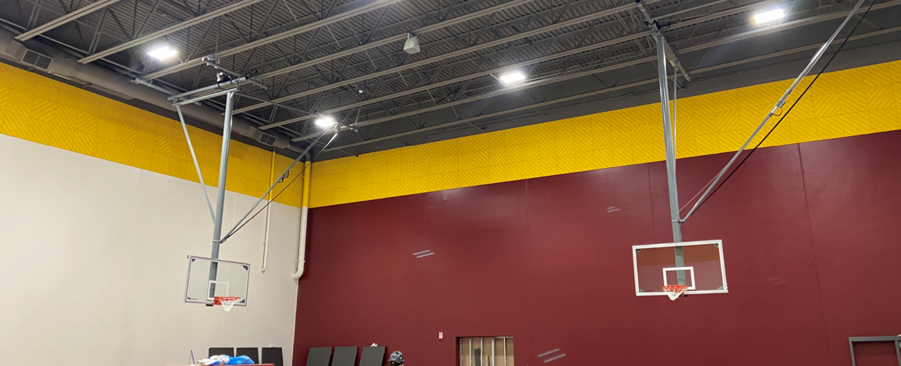 The basketball hoops are hanging in the gym. Soon they will receive their padding to show the completed look